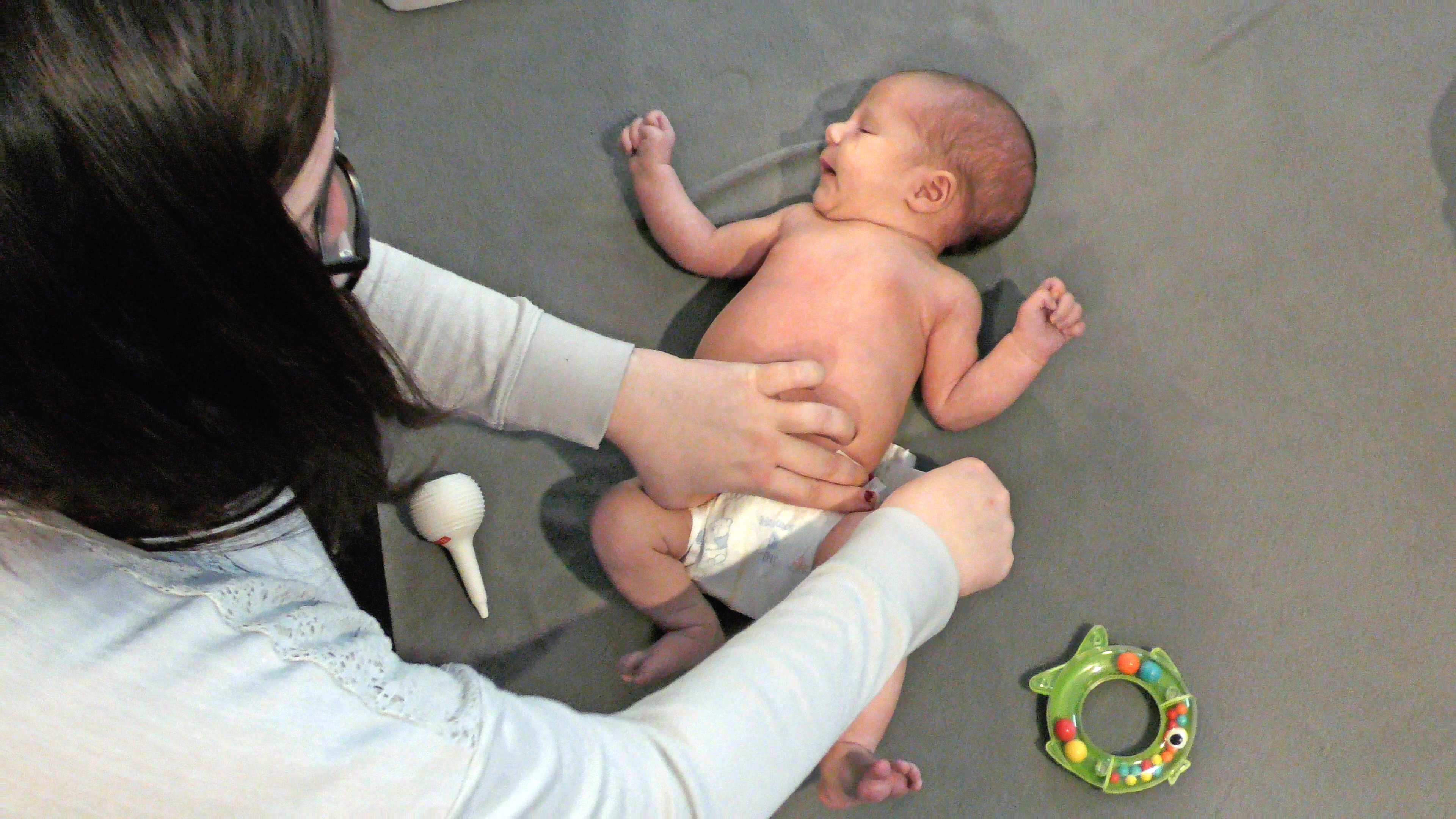 A mother leans over her baby on the floor as she puts a fresh diaper on them. A nasal aspirator and baby toy lie on either side of the baby’s legs.