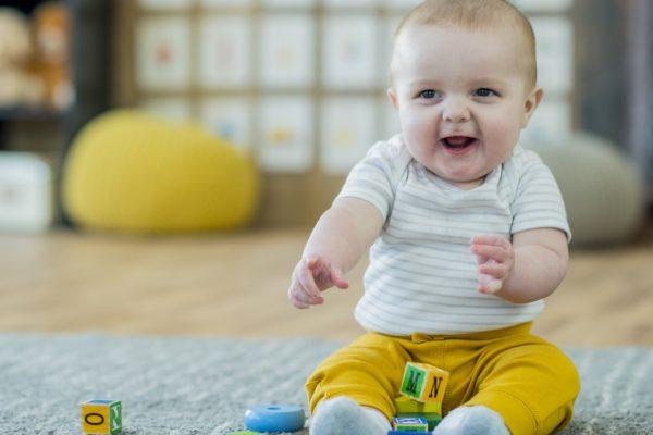 baby in yellow pants smiling and playing with blocks