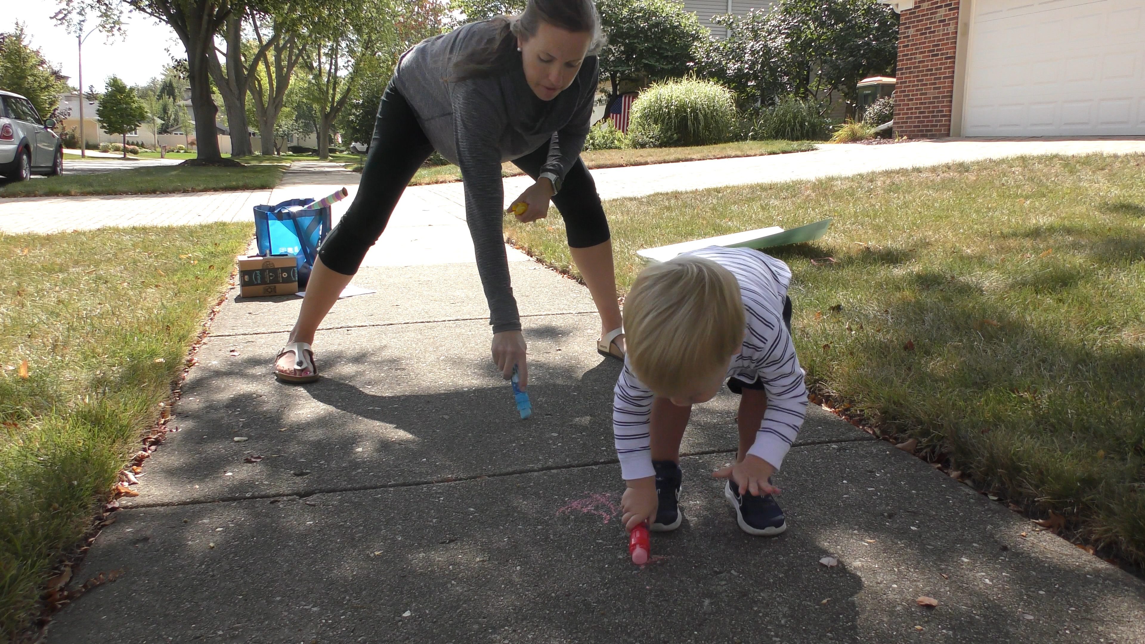 Mom and toddler boy doing a bear crawl while drawing with chalk on a sidewalk.
