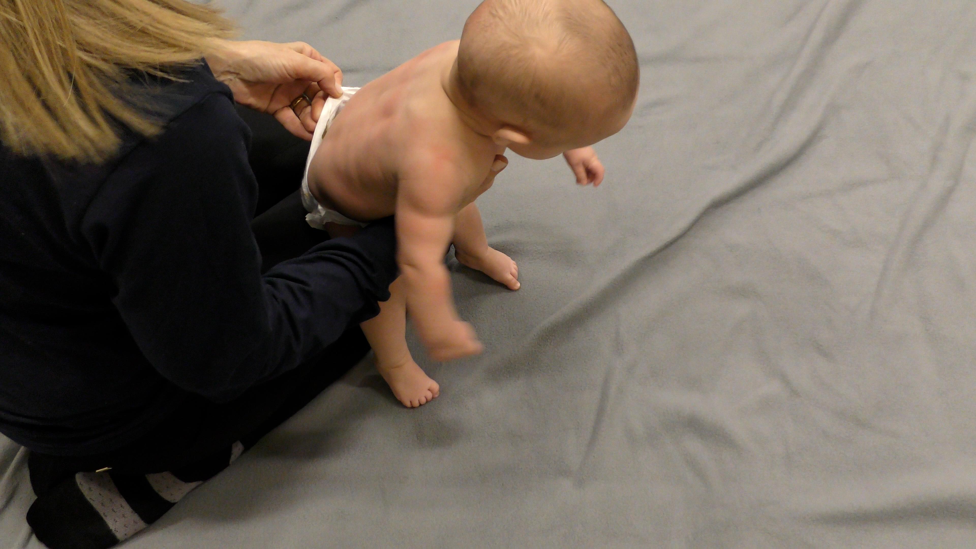 Mom checking Baby’s diaper while holding them upright on floor.