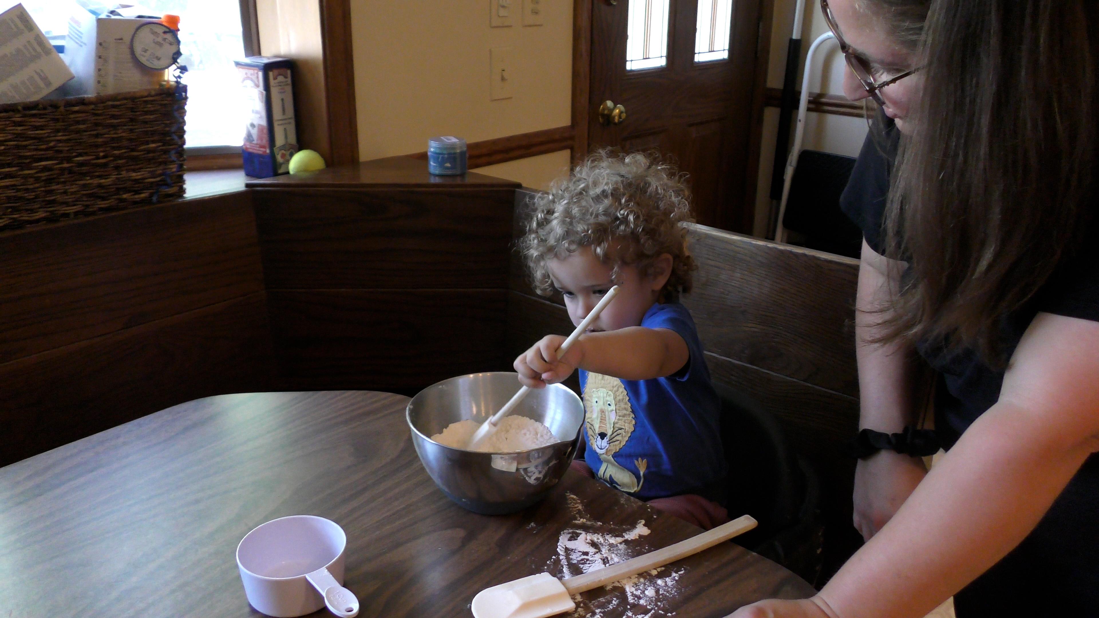 Mom letting toddler boy mix baking ingredients in a bowl by himself.