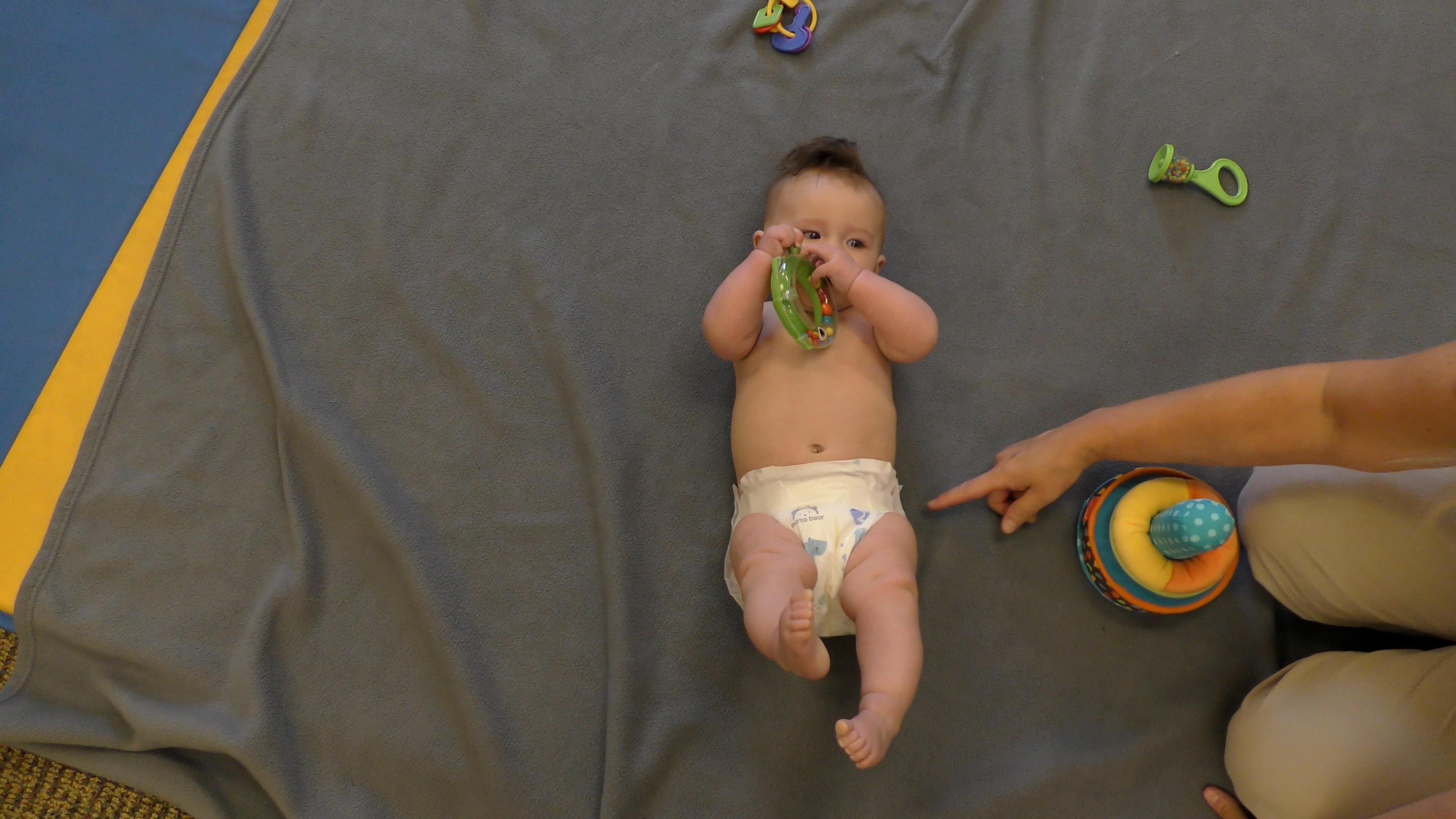  Baby in diaper lying of floor with off-screen adult pointing at diaper tabs.