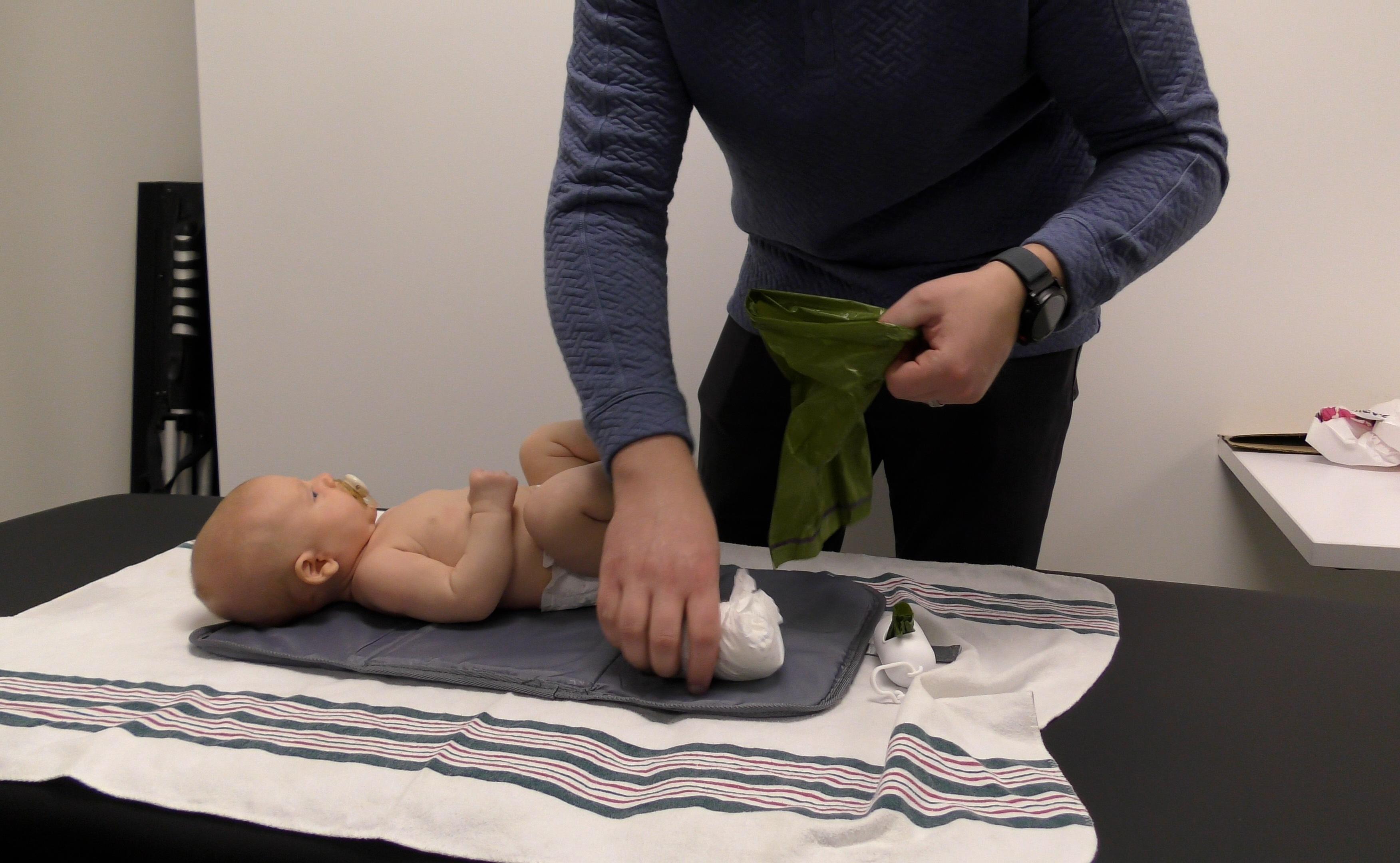 Dad changing Baby’s diaper on table with diaper changing pad beneath Baby.