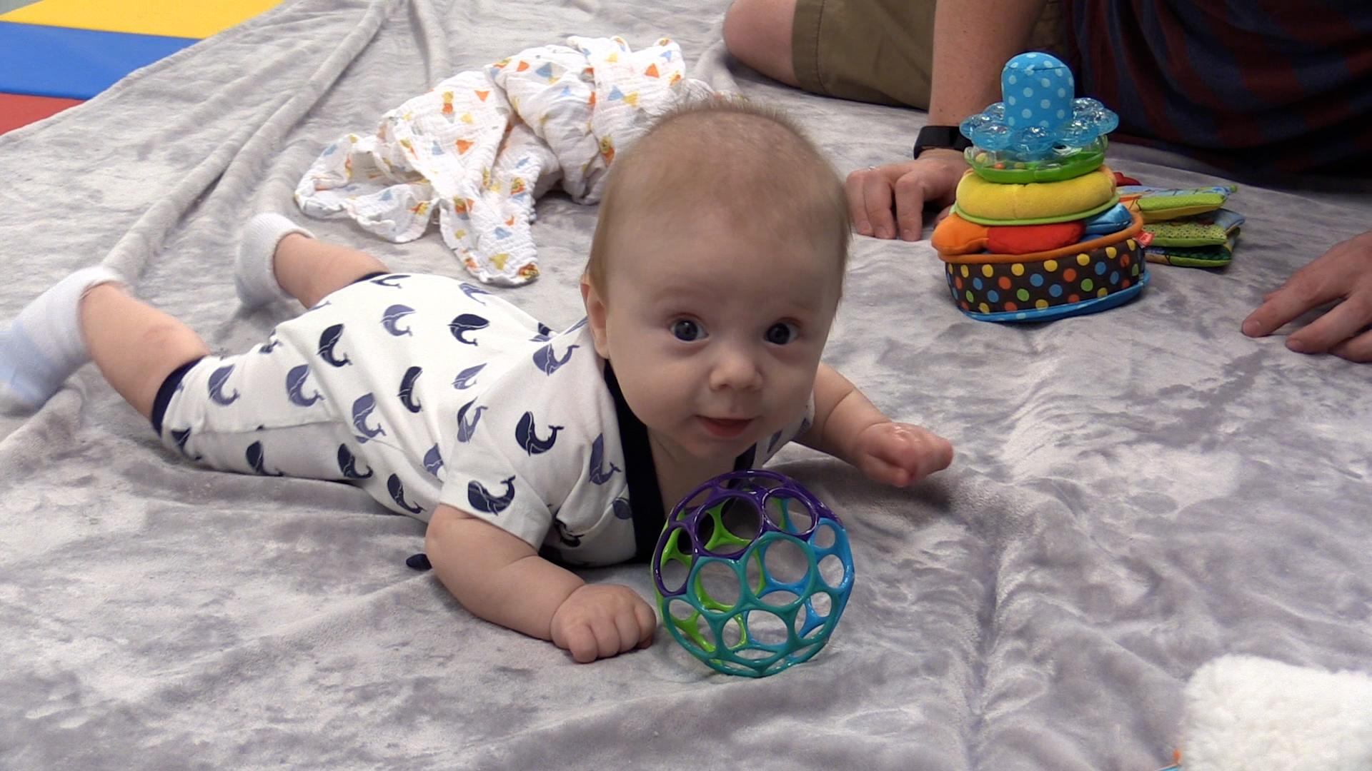 Parent getting Baby’s energy out by doing Tummy Time on the floor with toys.