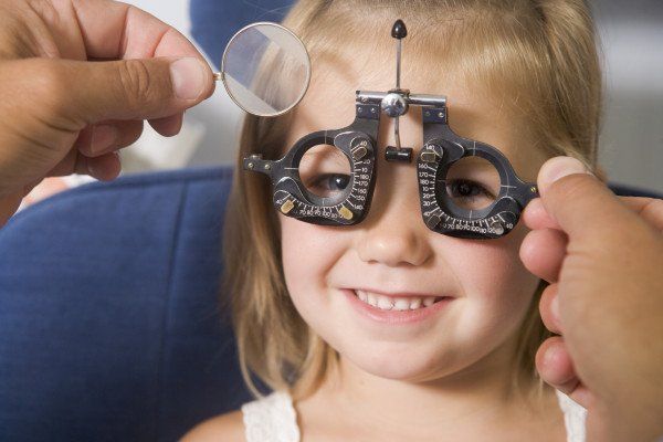 Optometrist in exam room with young girl in chair smiling