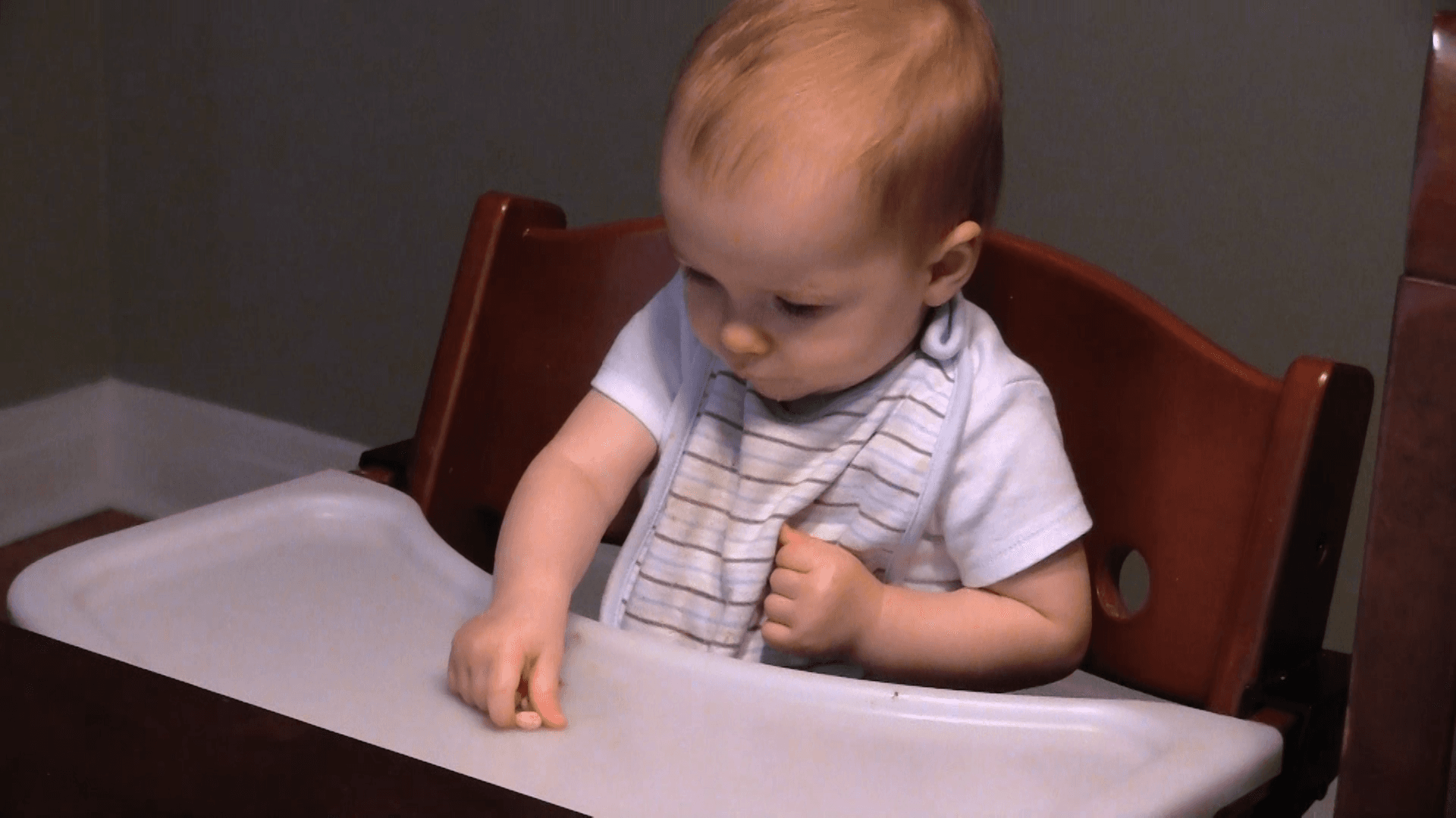 9-12-month-old baby using the pincer grasp to pick up a piece of cereal on his high chair tray.