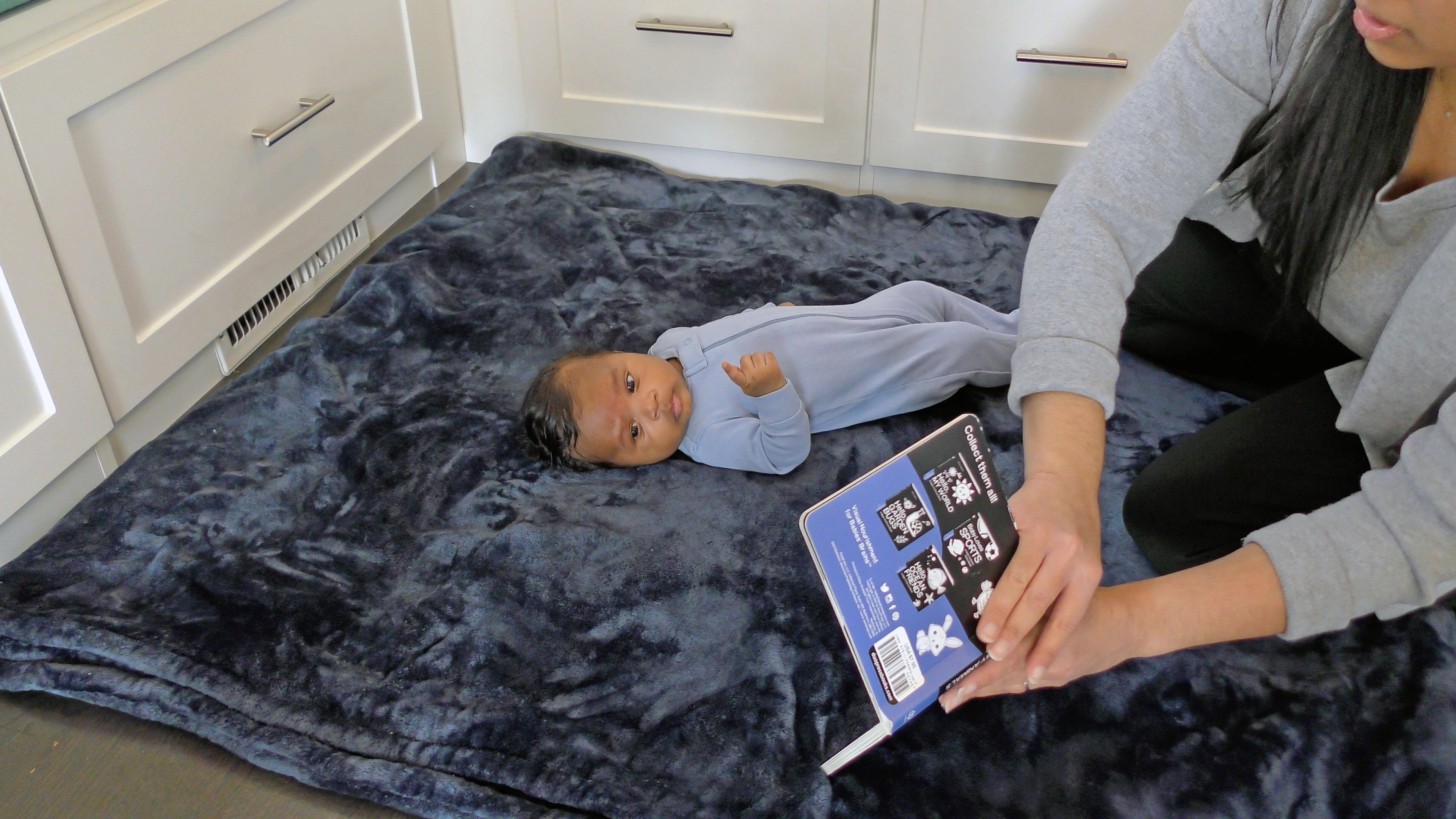 Caregiver using a book to get baby boy to turn his head to one side while lying on his back.