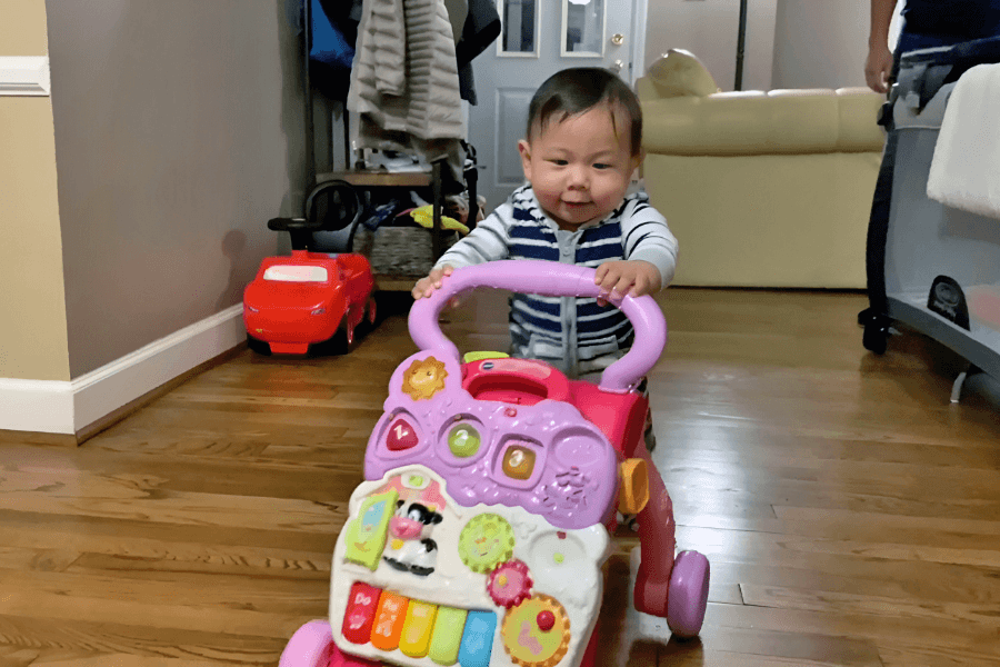 Baby walking while holding onto a multi-colored push toy.