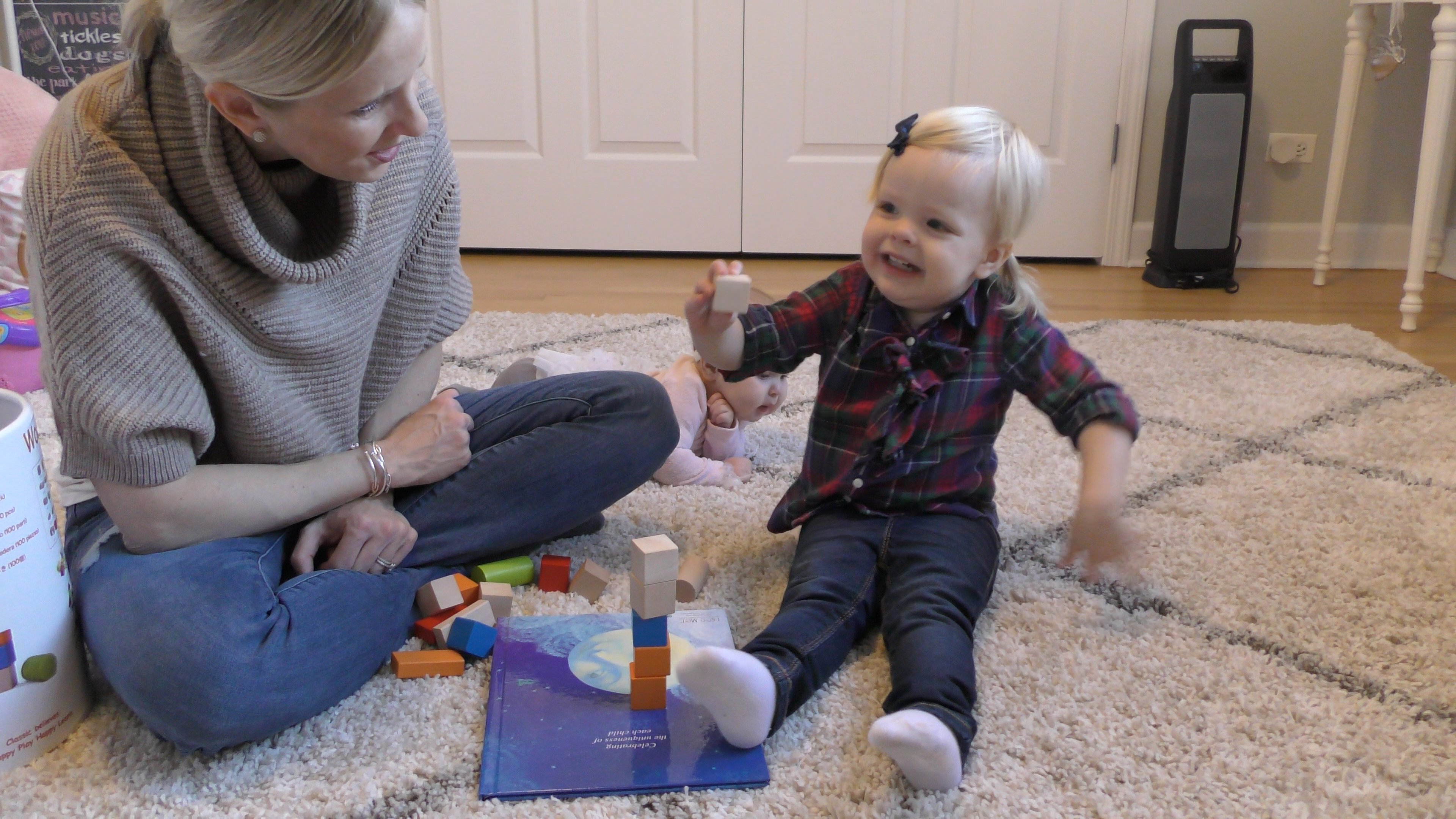 Toddler girl with a good attention span happily stacks blocks while her mother watches next to her.
