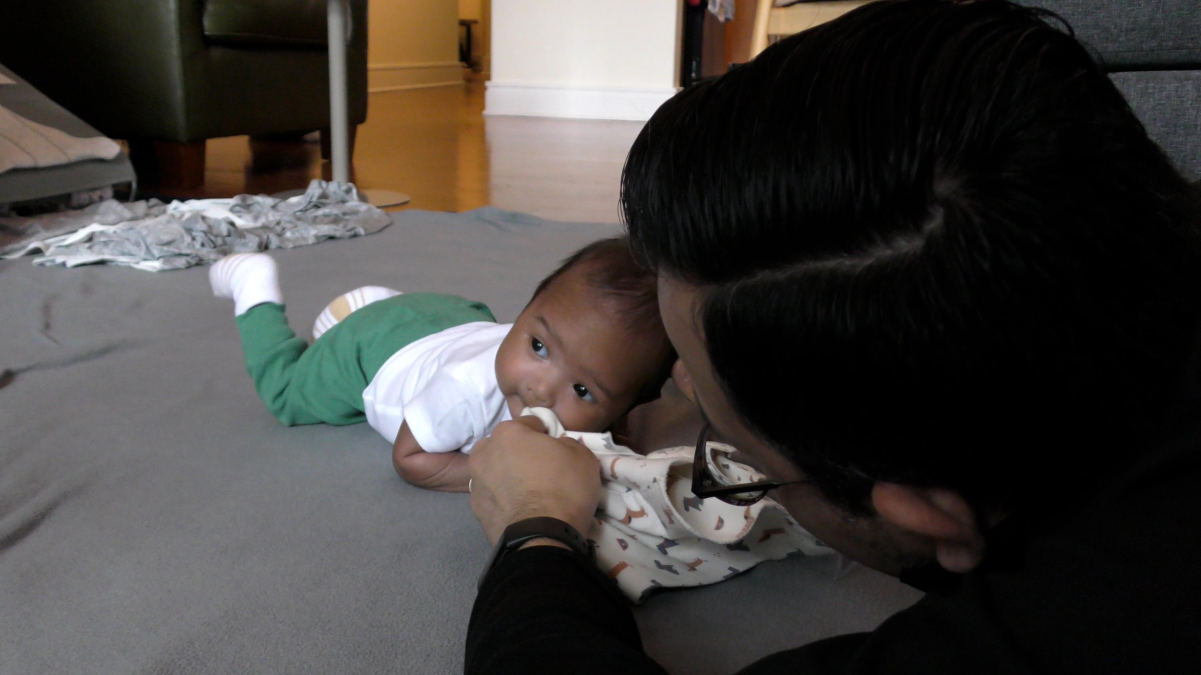Dad wiping baby boy’s nose with a dog print washcloth while baby does Tummy Time.