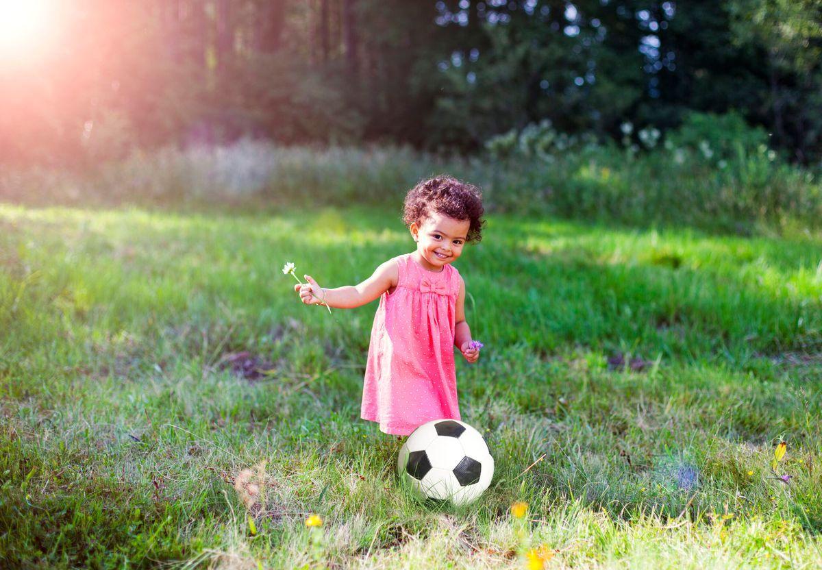 Child playing with a soccer ball outdoors to build motor skills and body awareness.