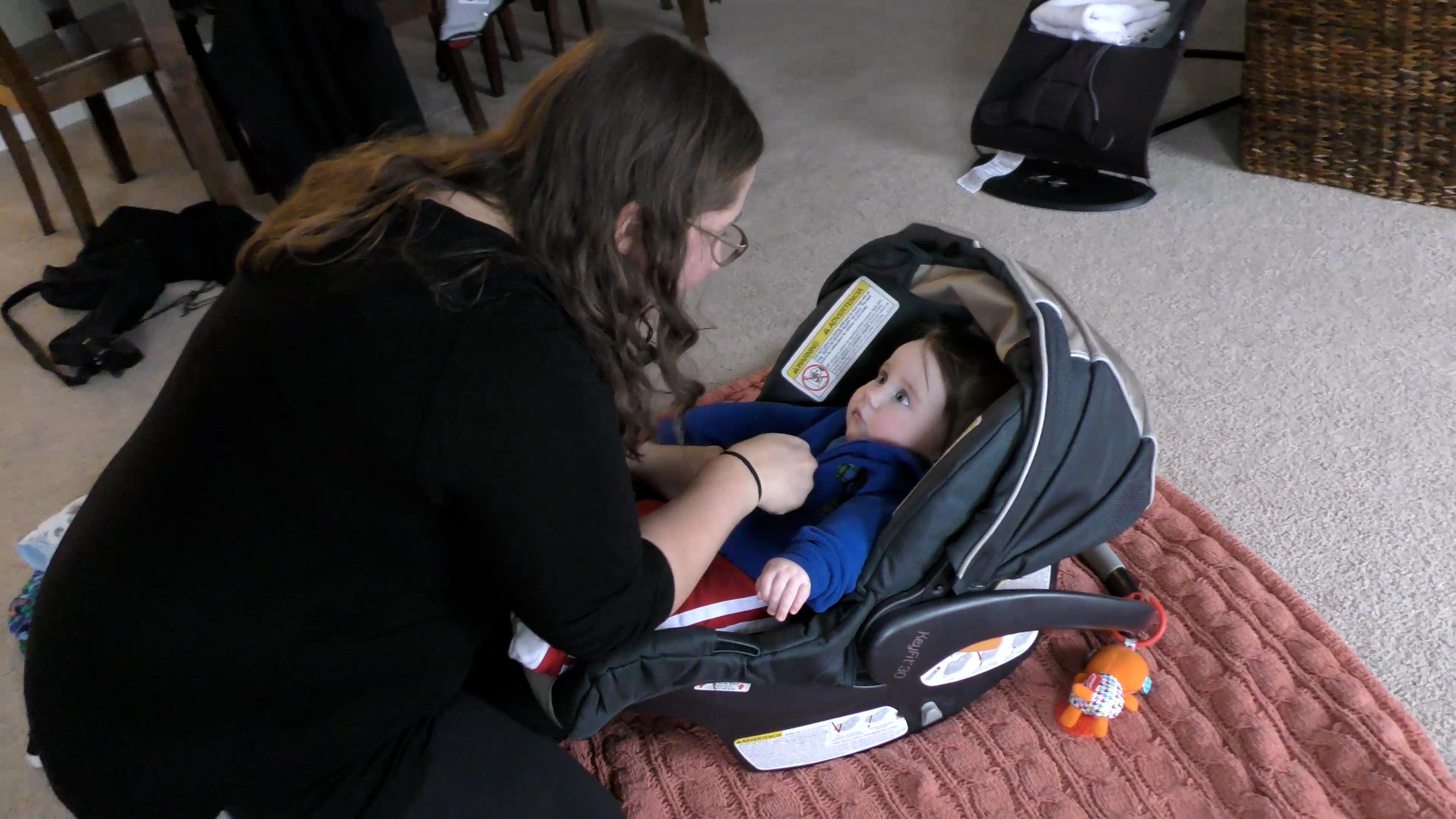 Mom preparing Baby for leaving the house by dressing him in layers and buckling him into his car seat.