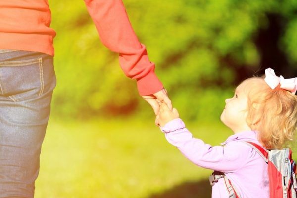 little_girl_holding_moms_hand_behind_outside