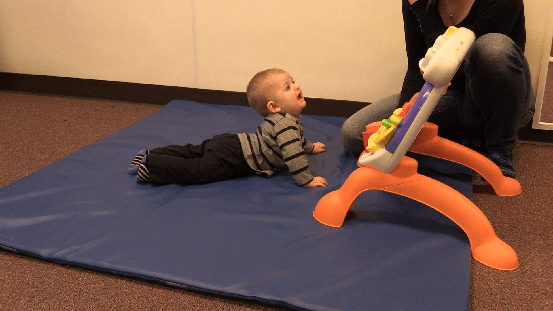 Baby looking up at caregiver with an upset look while doing Tummy Time on a playmat.