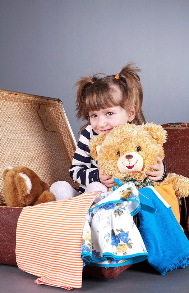 girl sitting in suitcase with toys and clothes