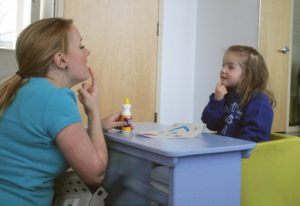 girl in speech therapy pointing her finger to mouth