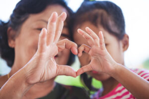 Asian grandmother and little child girl making heart shape with hands together with love
