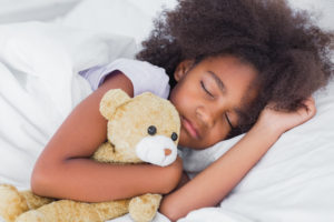 Cute little girl sleeping in bed cuddling teddy bear