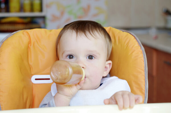 baby_holding_bottle_in_high_chair