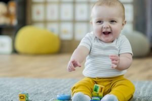 baby in yellow pants smiling and playing with blocks