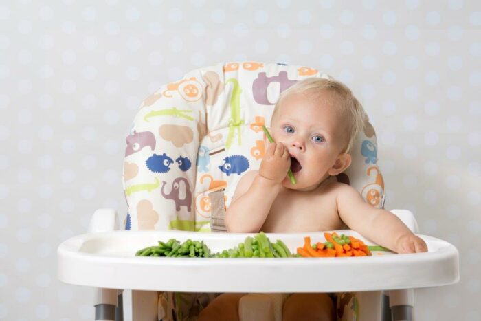 baby_in_high_chair_holding_vegetable