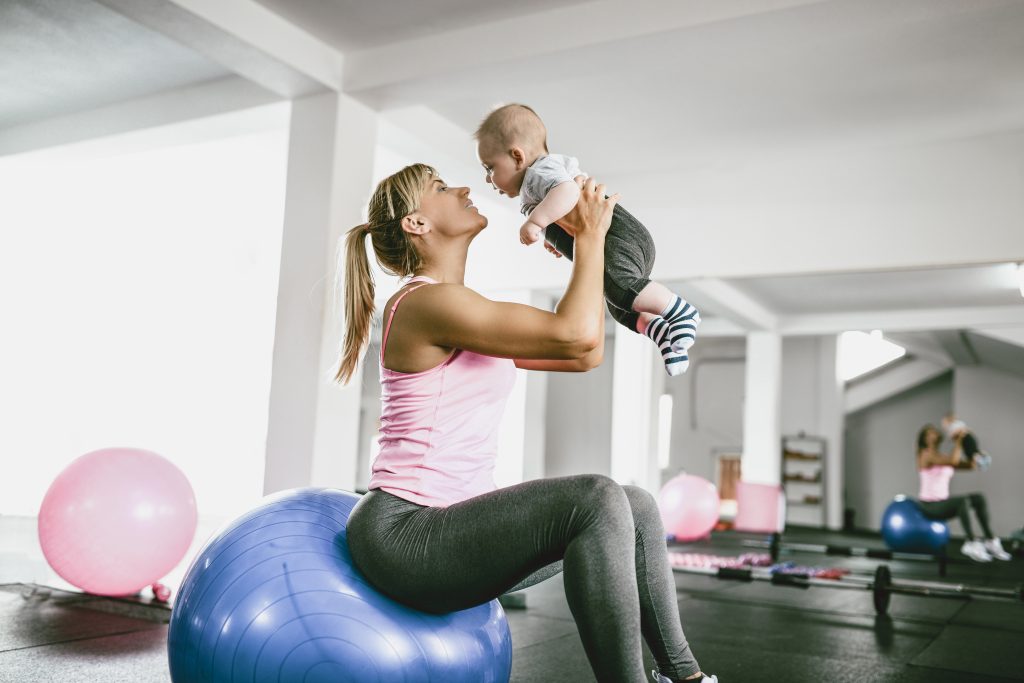  Athlete Mother Playing With Baby While Resting From Workout In Gym