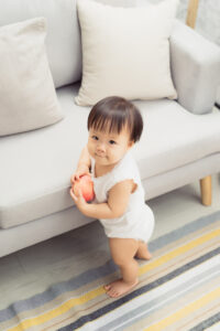 Cute little baby girl standing next to sofa at living room