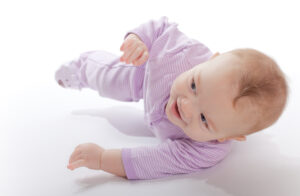 Six-months-old-baby-boy-in-a-striped-purple-baby-jumper-rolling-around-the-floor-with-a-smile